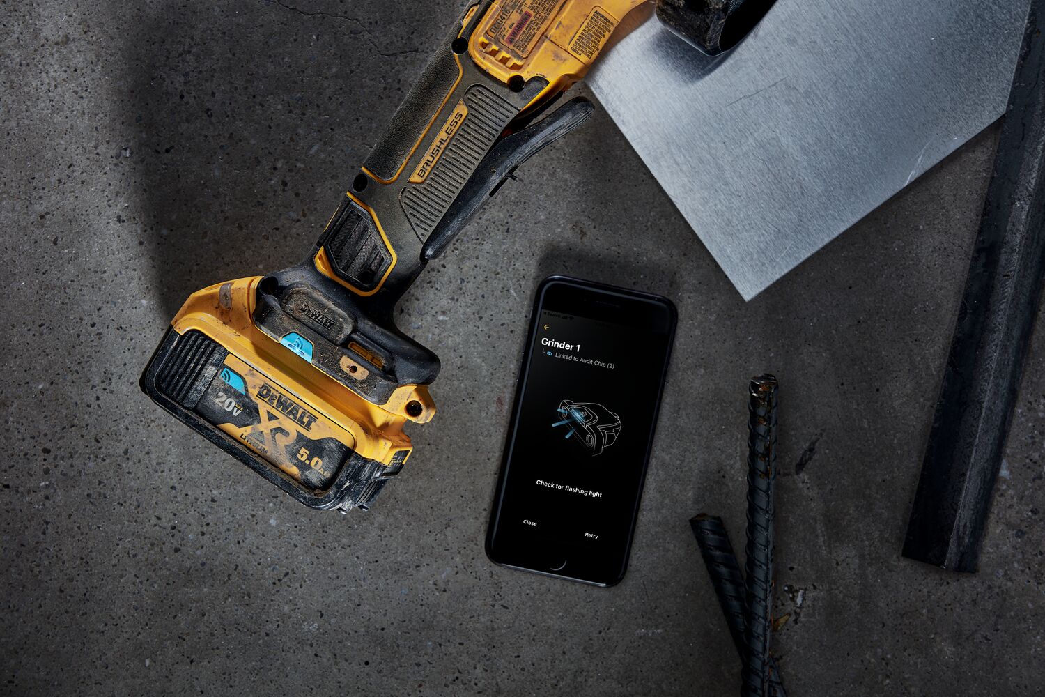 close up of the BRUSHLESS CORDLESS PADDLE SWITCH ANGLE GRINDER WITH FLEXVOLT ADVANTAGE placed on the floor with other tools and an iphone