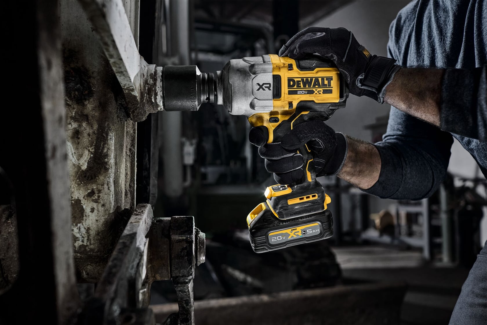 A person wearing gloves uses a DEWALT 20V XR cordless impact wrench to work on a large metal machine part in an industrial setting.