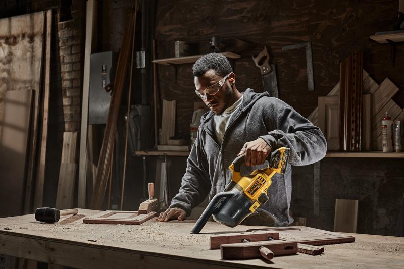 Male using DEWALT 20 MAX* Hand Vacuum vacuuming up wood dust, saw dust, wood chips. DEWALT Power Stack battery is being used.